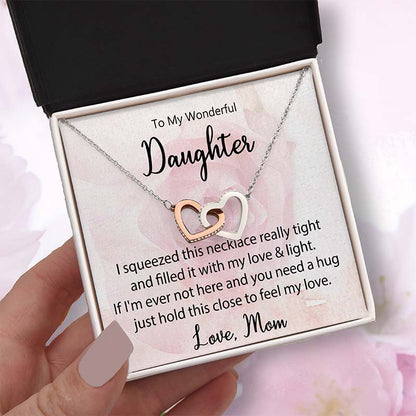 Two-tone interlocking heart necklace displayed in a gift box with a heartfelt daughter message card from Mom, held in hand against a soft pink floral background
