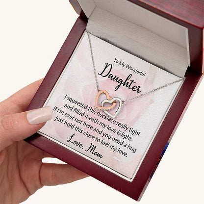 Two-tone interlocking heart necklace displayed in a gift box with a heartfelt daughter message card from Mom, held in hand against a white background