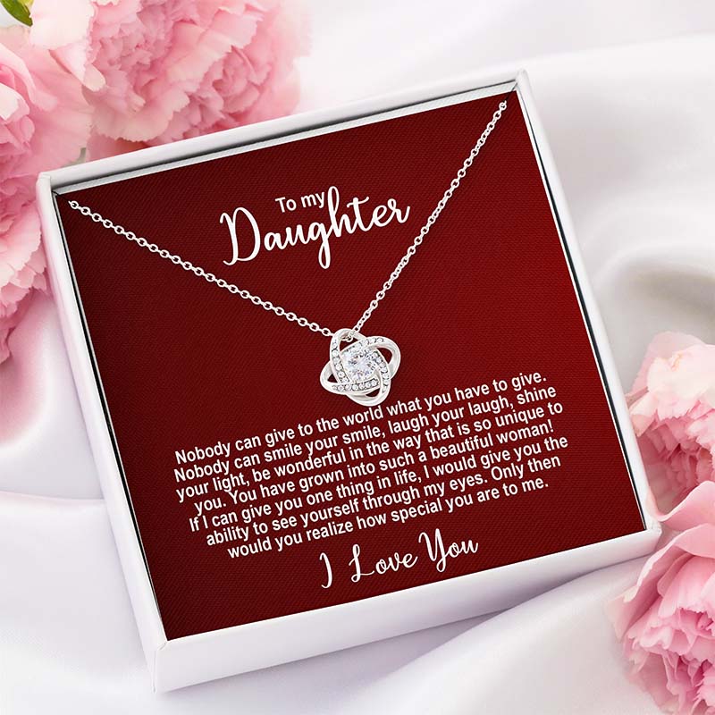 Silver knot necklace in a box with personalized message addressed to a daughter on a red card shown in a white gift box against a white silk with pink flowers background.
