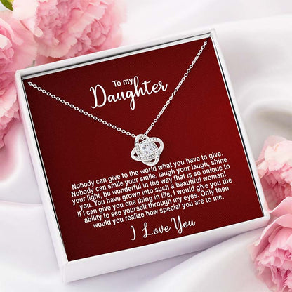 Silver knot necklace in a box with personalized message addressed to a daughter on a red card shown in a white gift box against a white silk with pink flowers background.