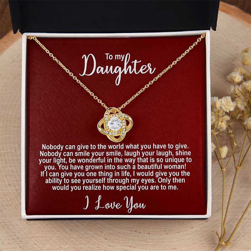 Gold knot necklace in a box with a sentimental message for a daughter on a red card displayed on a wooden surface.