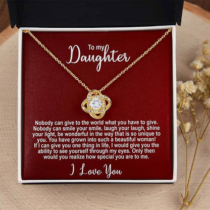 Gold knot necklace in a box with a sentimental message for a daughter on a red card displayed on a wooden surface.