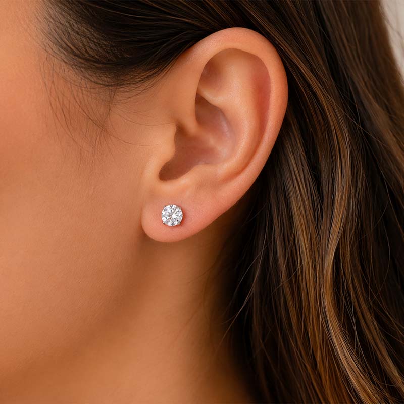 Woman wearing a round cubic zirconia stud earring with a silver-tone setting.