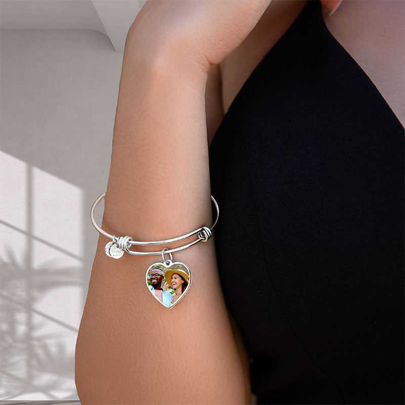 Silver bracelet with a heart-shaped photo charm on a person's wrist.