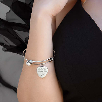 Silver bracelet with a heart-shaped tag on a wrist against a black background