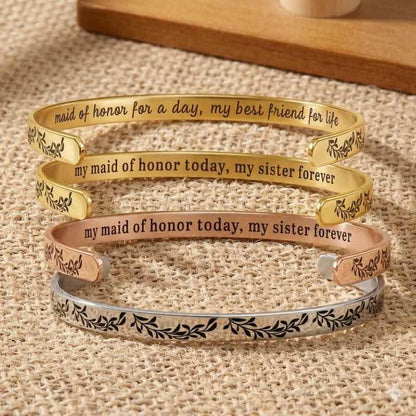 Three gold, rose gold, and silver bracelets with engraved text on a textured surface.