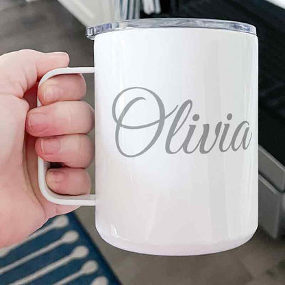 Hand holding a white custom engraved insulated stainless steel coffee mug personalized with "Olivia" in elegant script, featuring a clear press-in lid.