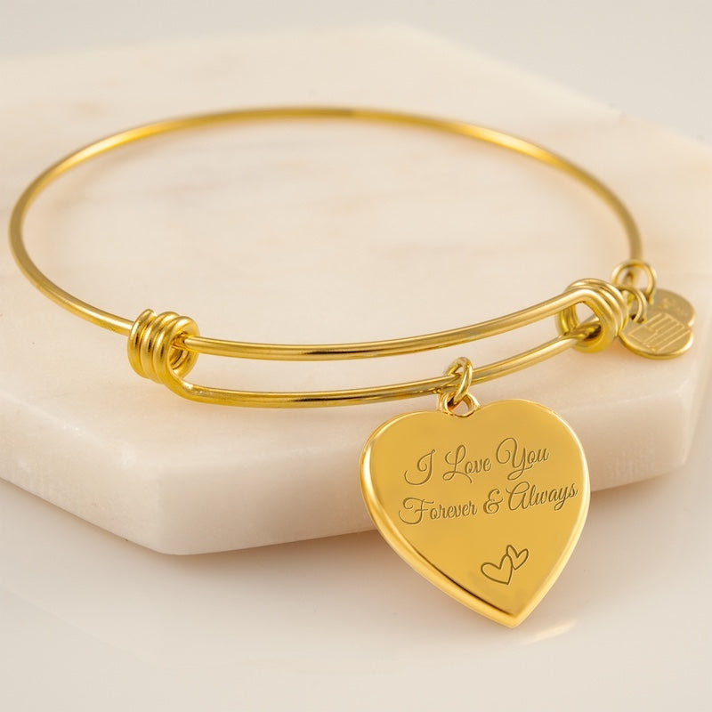 Engraved bracelets for women: Gold bracelet with a heart-shaped tag engraved with 'I Love You Forever & Always' on a beige background.