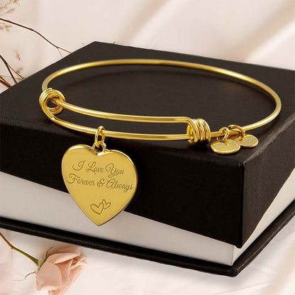 Gold personalized bracelet with heart-shaped charm on a black box with flowers in the background