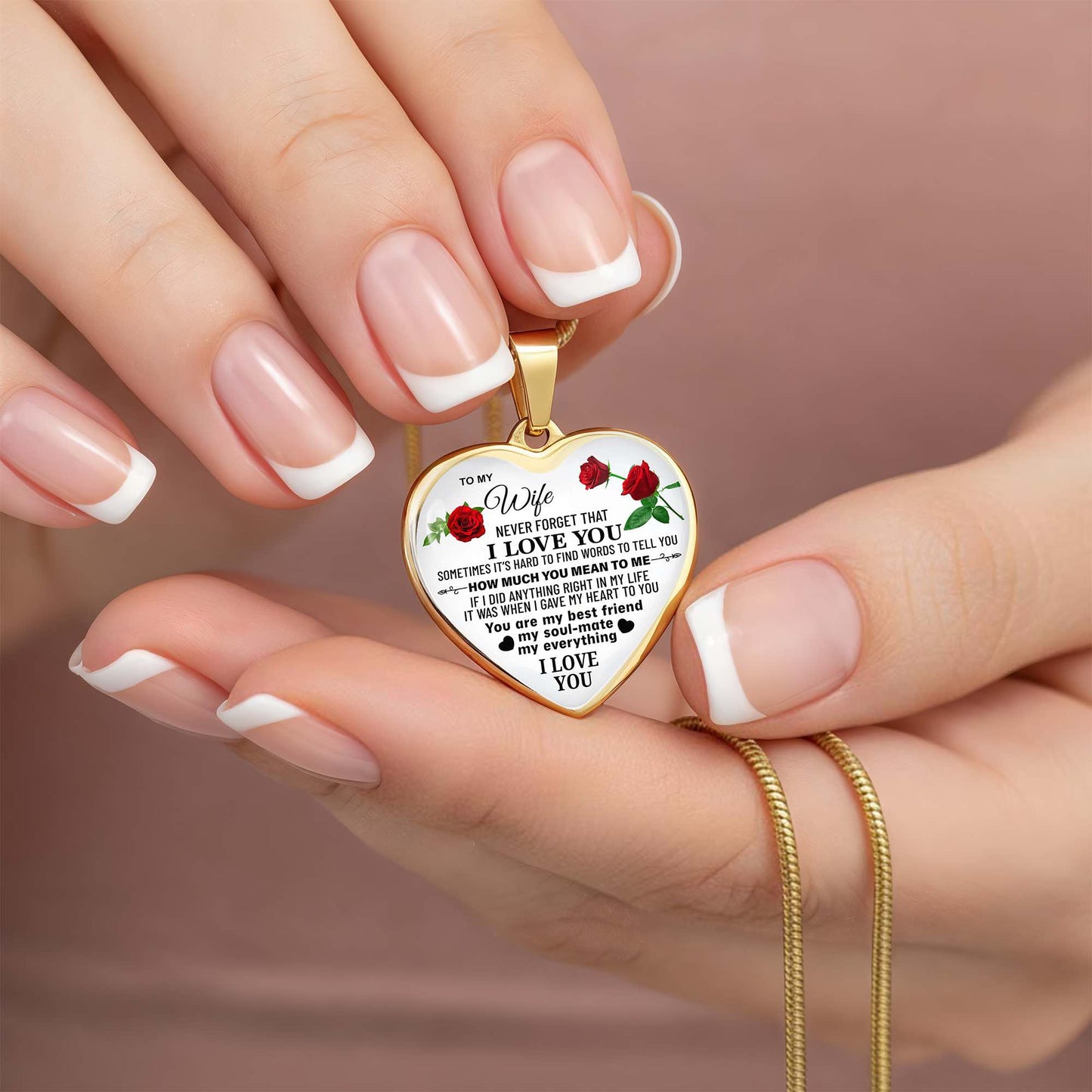 Engraved gold heart necklace with a romantic message for wife and red rose accents on a silver snake chain, shown in close-up, held by hands.