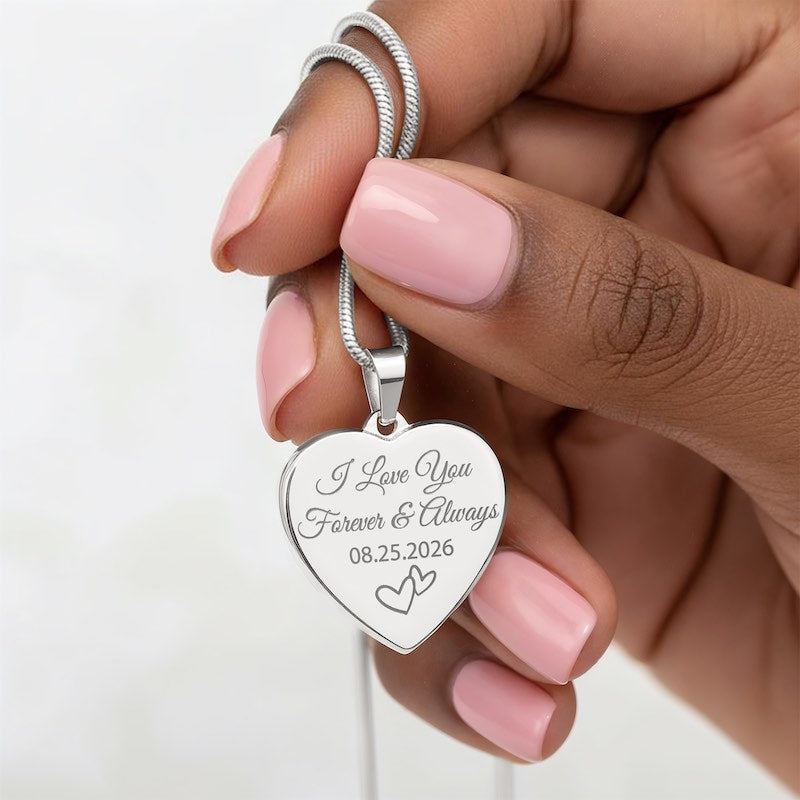 Silver heart pendant engraved with "I Love You Forever & Always," a custom date, and heart illustrations on a silver snake chain, held by a hand.