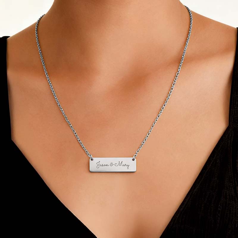 A silver bar necklace with personalized engraving reading 'Jason & Mary' worn on a model's neck over a black top.