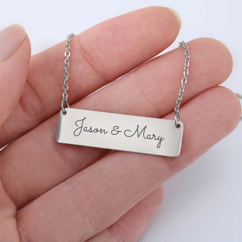 Silver bar necklace with text engraving held in a hand against a white background
