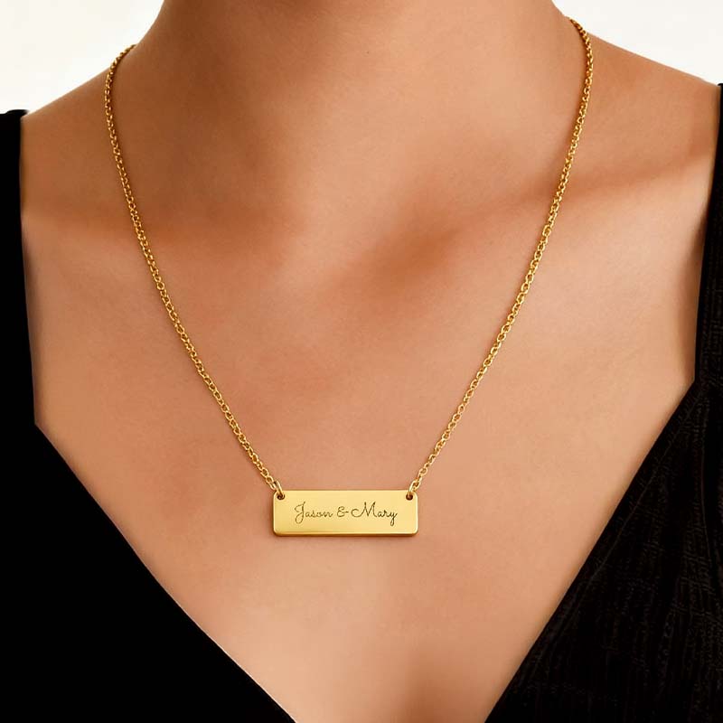 A gold bar necklace engraved with 'Jason & Mary' worn on a model's neck, styled with a black V-neck top.