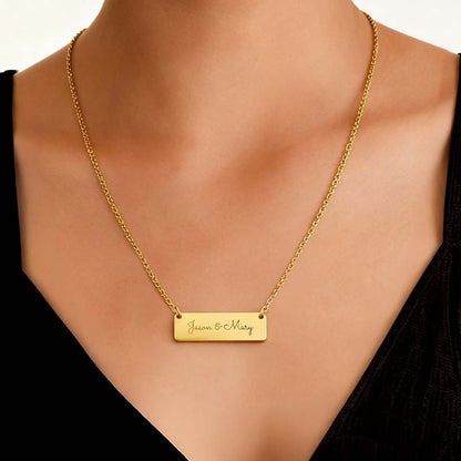 A gold bar necklace engraved with 'Jason & Mary' worn on a model's neck, styled with a black V-neck top.