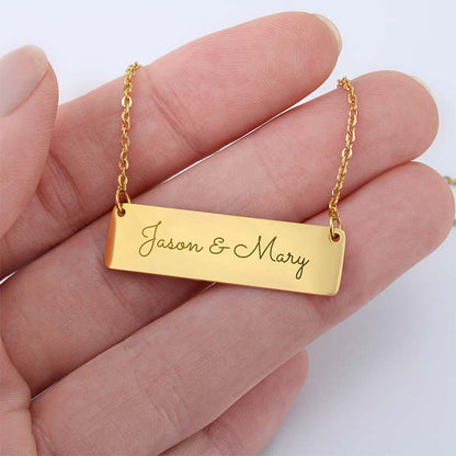 A gold rectangular nameplate necklace engraved with 'Jason & Mary', held in a person's hand against a clean white background.