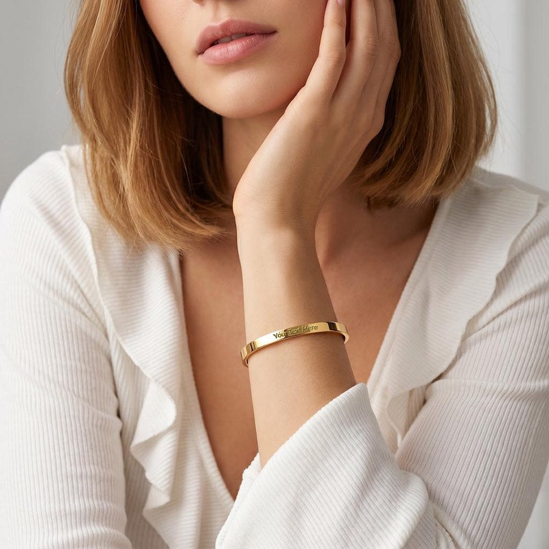 Model wearing a custom gold cuff bracelet with engraved text area, wearing a white long-sleeve top.
