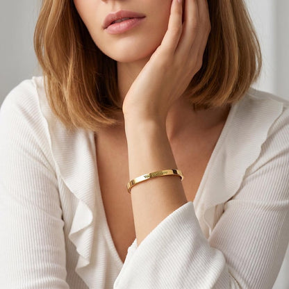 Model wearing a custom gold cuff bracelet with engraved text area, wearing a white long-sleeve top.