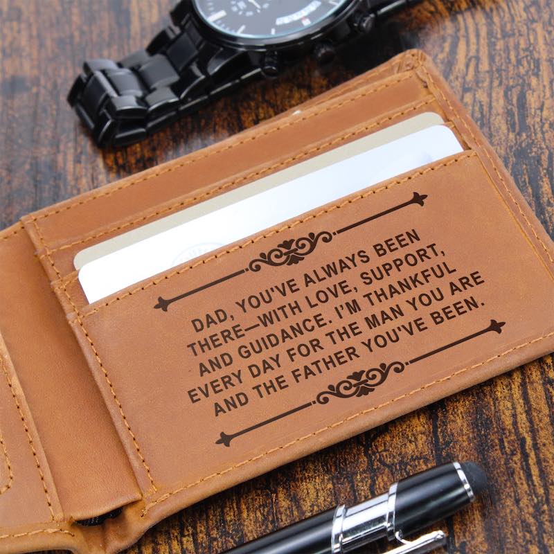 Open tan leather wallet on a wooden surface beside a black watch and pen, featuring card slots engraved with a message to Dad: "Dad, you've always been there—with love, support, and guidance..."   