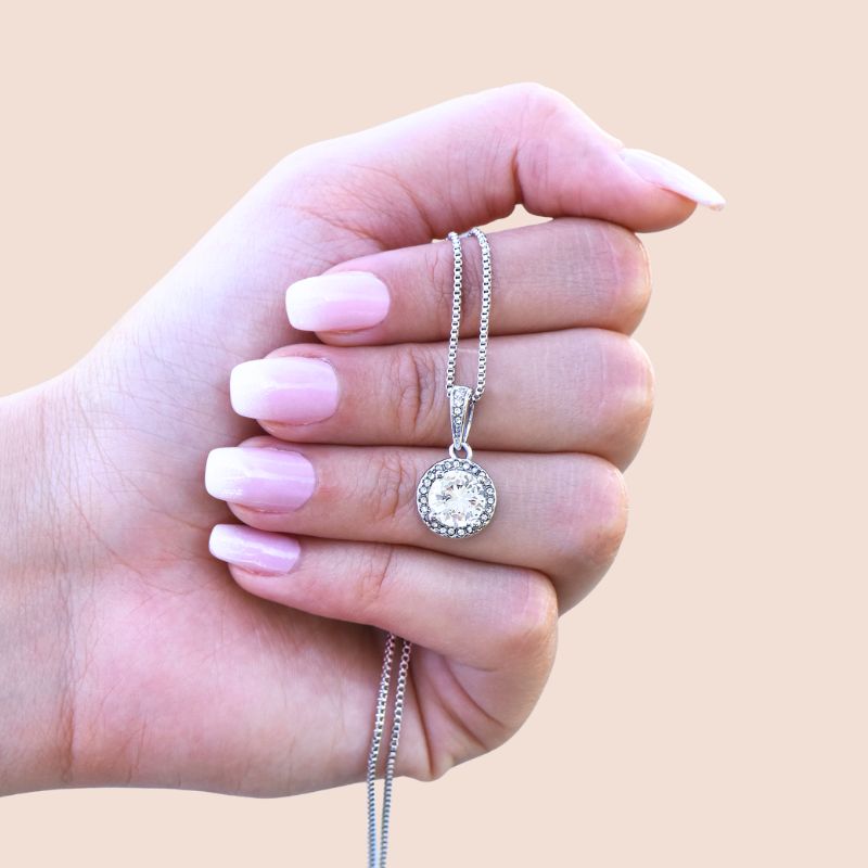 retirement gift ideas for a female - Hand holding a silver necklace with a round pendant against a beige background 