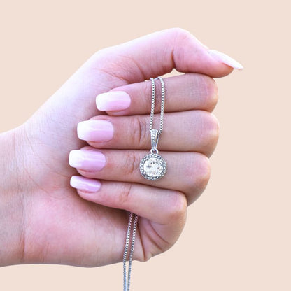 retirement gift ideas for a female - Hand holding a silver necklace with a round pendant against a beige background 