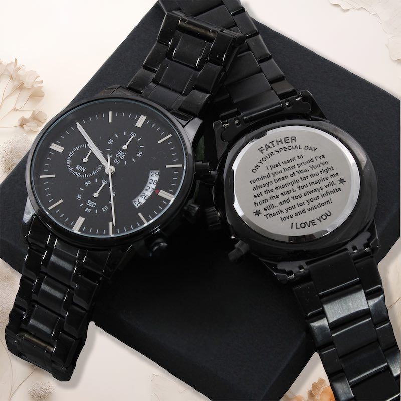 father watches: Two black metal link wristwatches arranged on a black surface. One watch face is visible and the other is turned over to show a engraved backplate message for Father's Birthday.