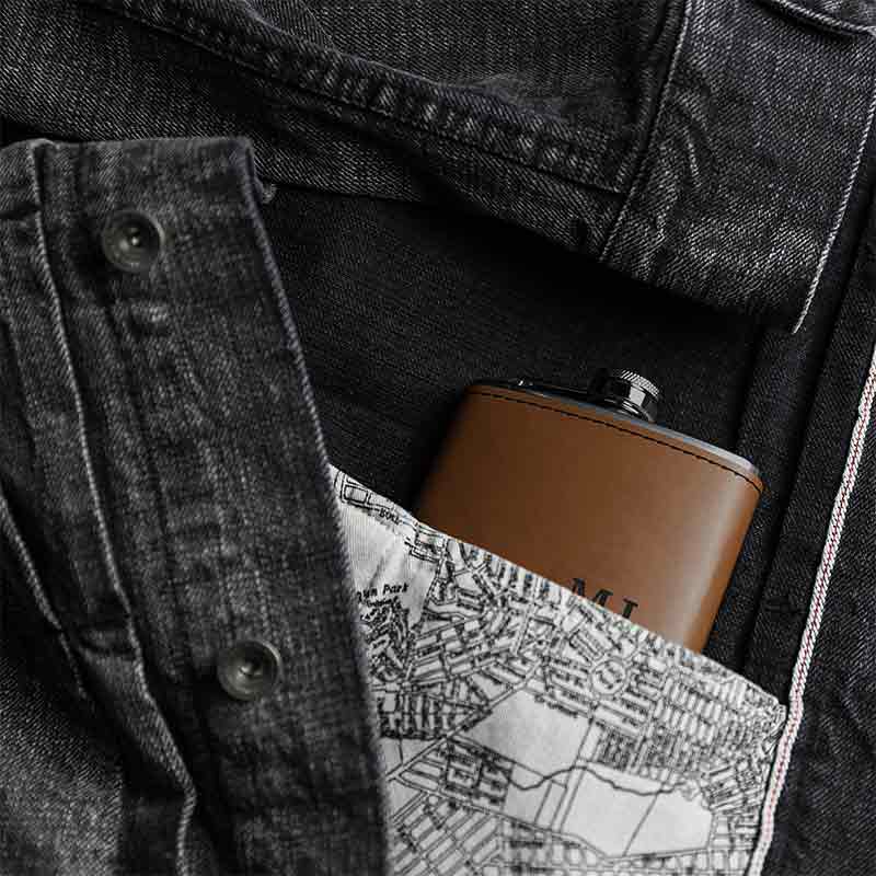 Rawhide custom engraved stainless steel flask tucked inside a dark denim jacket pocket.