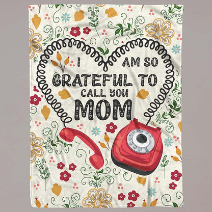 Blanket with floral design and text 'I am so grateful to call you Mom' featuring a red phone, on a grey background