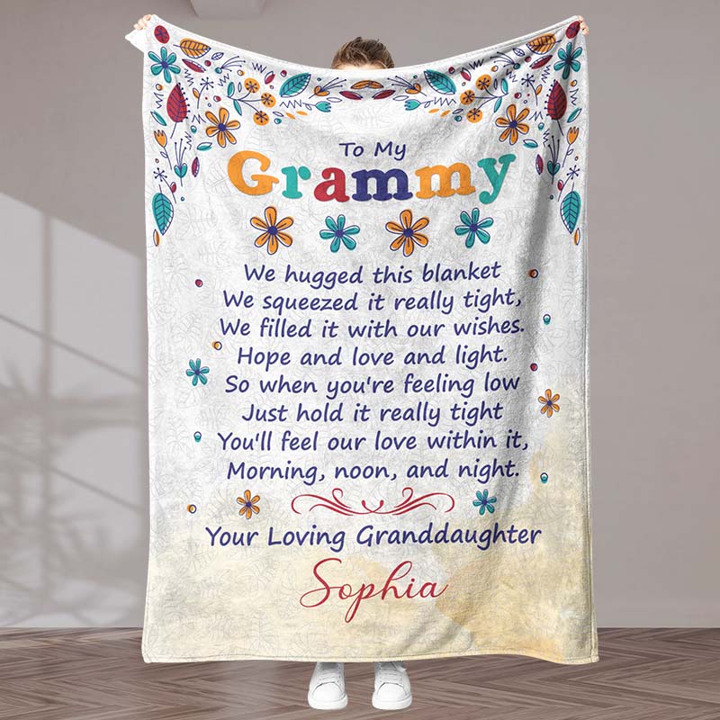 Beige blanket with floral design and sentimental text 'To My Grammy', held by a person, in an indoor background.