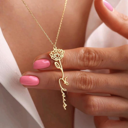 Gold necklace with a flower pendant held by a hand with pink nail polish.