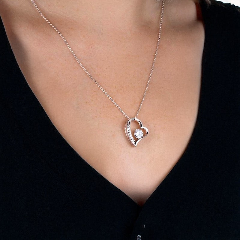 Silver heart-shaped necklace with a pendant with a round cut Cubic Zirconia stone on a person wearing a black top.