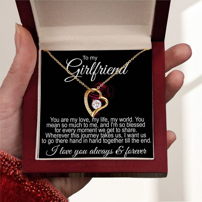 Unique gifts for girlfriend: A luxury mahogany-style gift box held in a person's hands, containing a gold heart-shaped necklace with a central crystal and a romantic message card addressed "To my Girlfriend".   