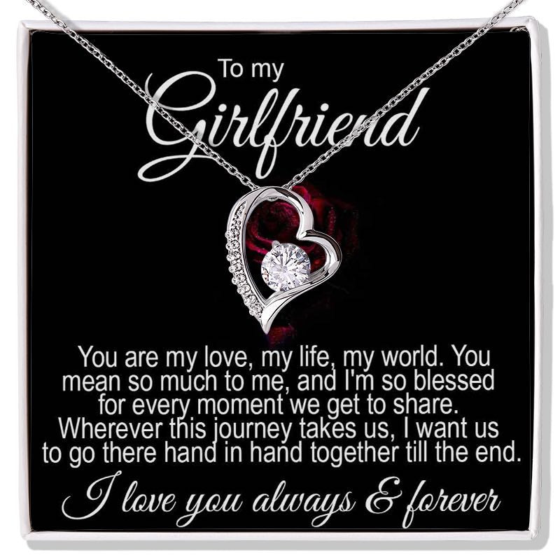 Gifts for Girlfriend: A silver heart-shaped necklace featuring a round sparkling crystal at its center, presented inside a black gift box. Above and below the necklace is a printed romantic message addressed "To my Girlfriend," expressing love and commitment.   