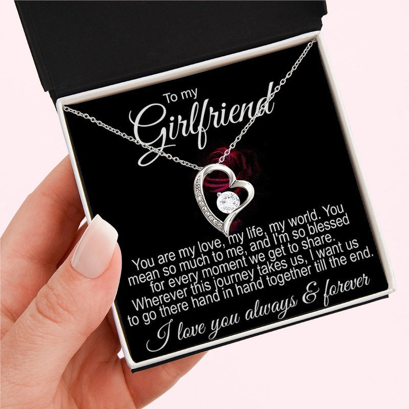 Necklace for girlfriend: A hand holding an open black gift box containing a silver heart-shaped necklace with a central crystal and a romantic "To my Girlfriend" message card.   