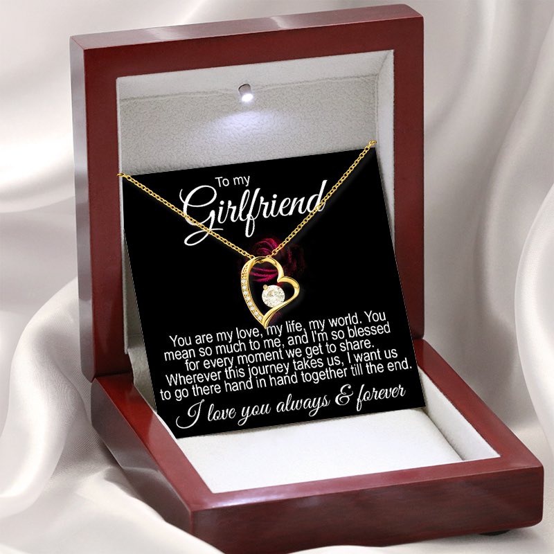 An illuminated luxury mahogany-style gift box displaying a gold heart-shaped necklace with a central sparkling crystal and a romantic "To my Girlfriend" message card.   