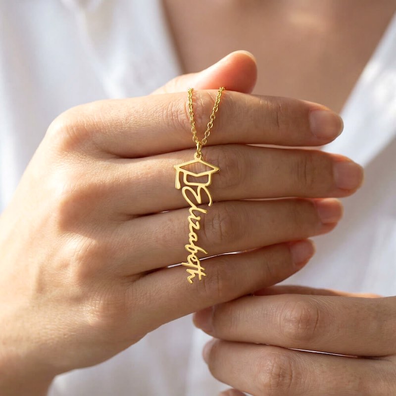 Gold necklace with 'Elizabeth' pendant held by a hand against a white background