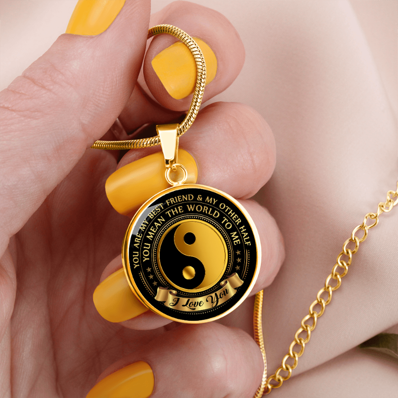 Gold necklace with a black and gold design Yin Yang on pendant, held by a hand with yellow nail polish.