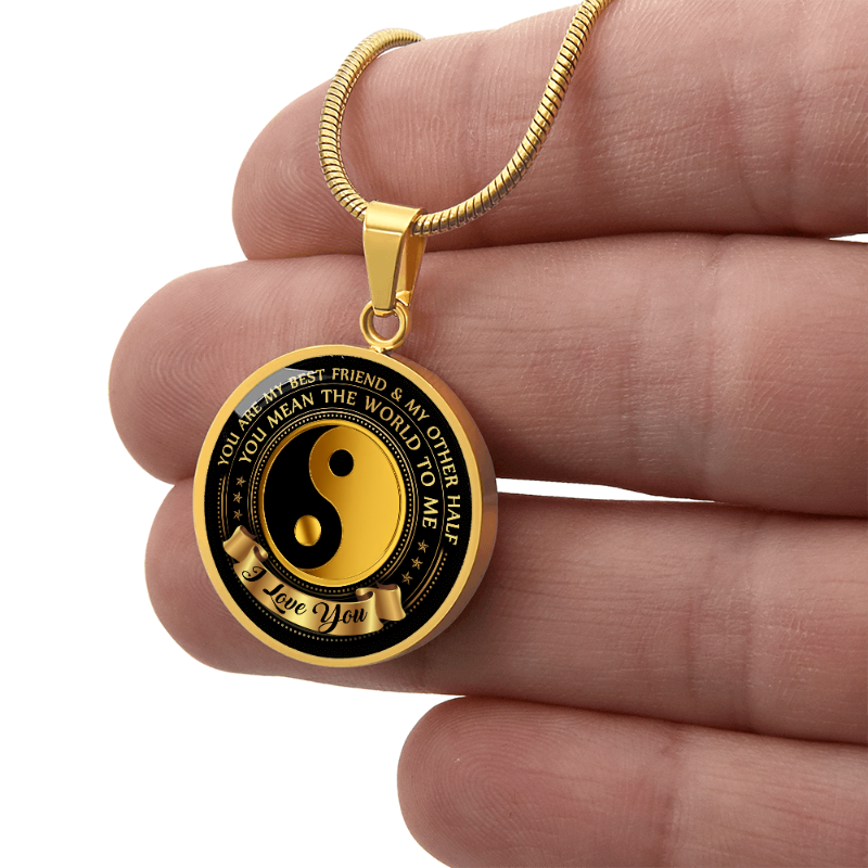 Gold round pendant yin yang with engraving, held between fingers on a white background