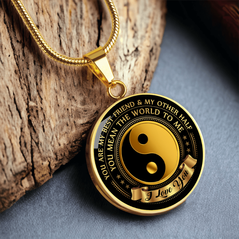 Gold and black pendant with yin yang symbol and engraved text on a wooden surface
