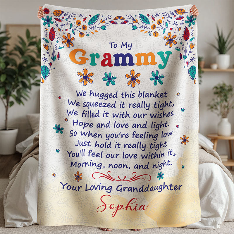 Decorative beige blanket with colorful flower design and heartfelt message for Grammy, from granddaughter, held by a person, in a bedroom setting.