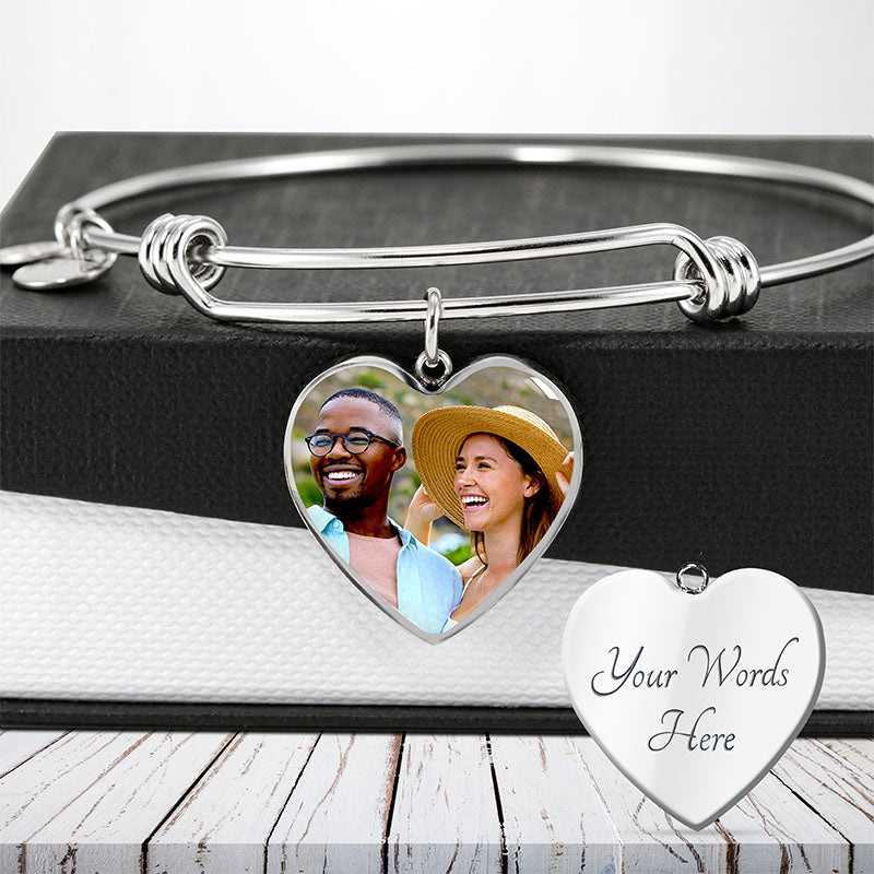 Silver heart-shaped engraved photo bracelet and customizable message tag on a wooden surface.