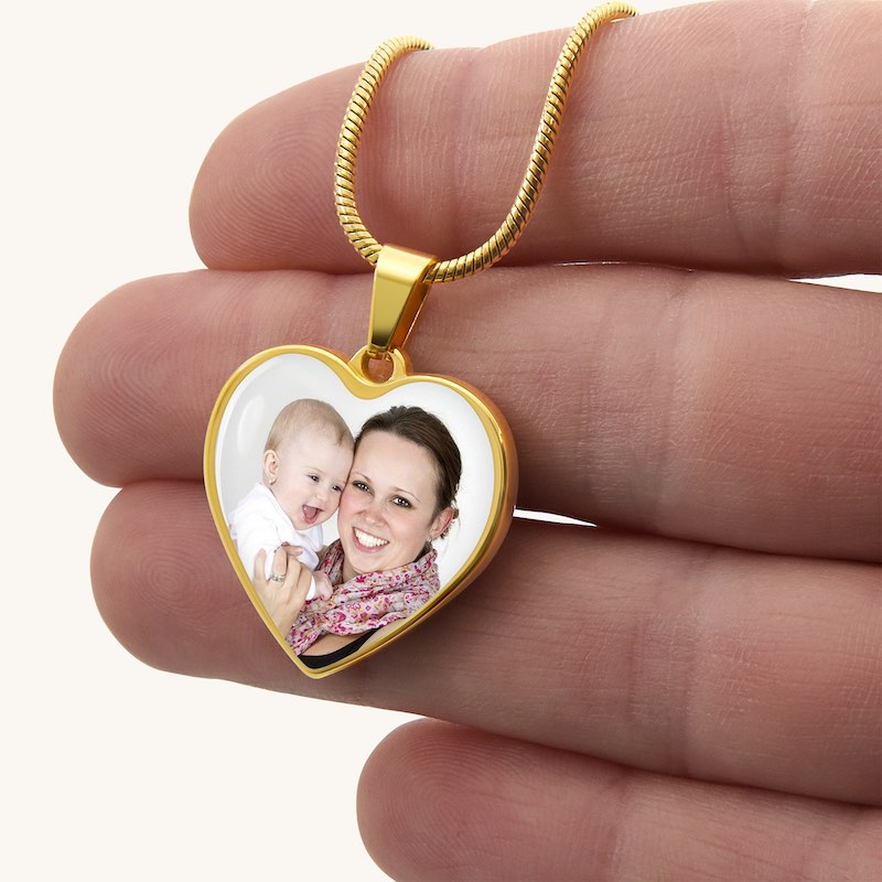 Heart-shaped pendant with a photo of a woman and a baby held between fingers