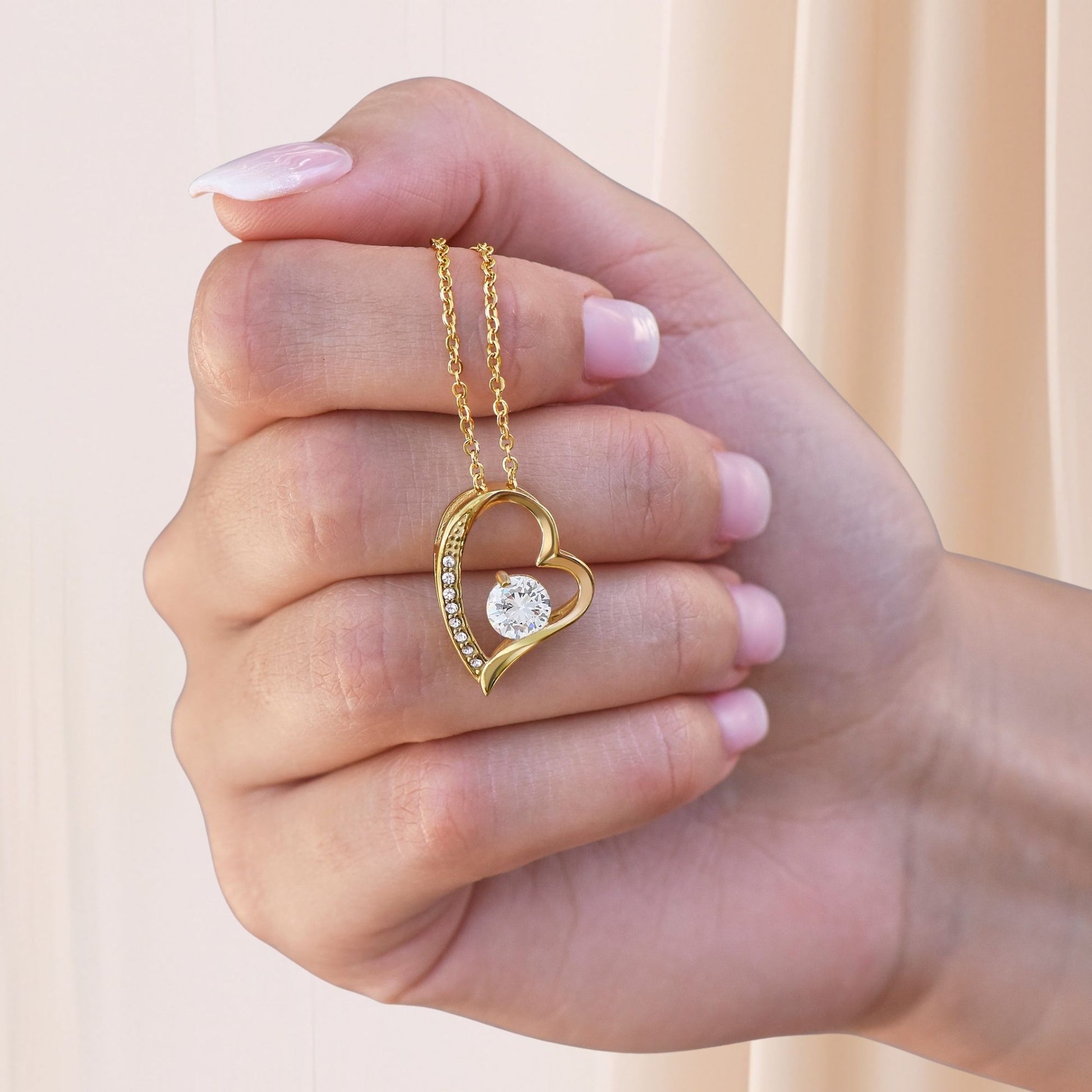 Gold heart necklace with a heart-shaped pendant featuring a round cut Cubic Zirconia stone in the center and small CZ around the pendant, held in a hand against a light background