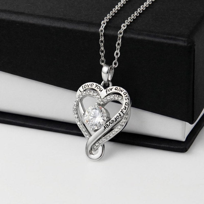 Heart-shaped silver necklace with a clear cubic zirconia stone on a black and white gift box.