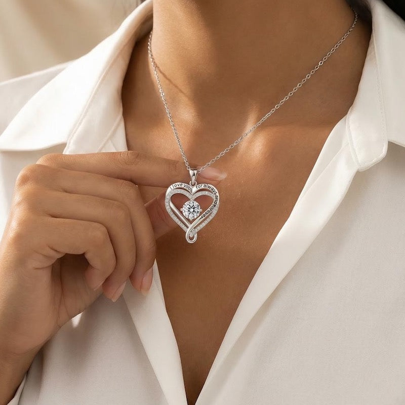 Silver heart-shaped necklace with a cubic zirconia crystal centered stone on pendant worn by a person in a white shirt.