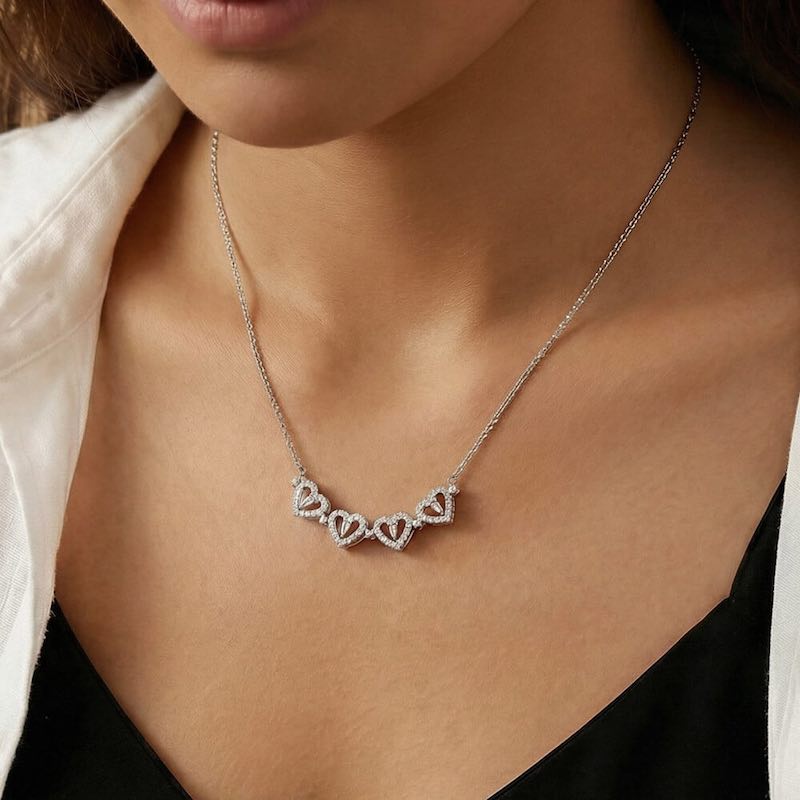 Silver necklace with heart-shaped pendant on a person wearing a white shirt.