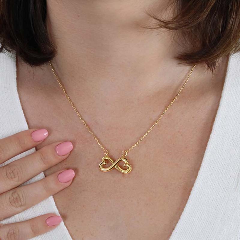 Gold infinity heart necklace worn by a model in a white top.