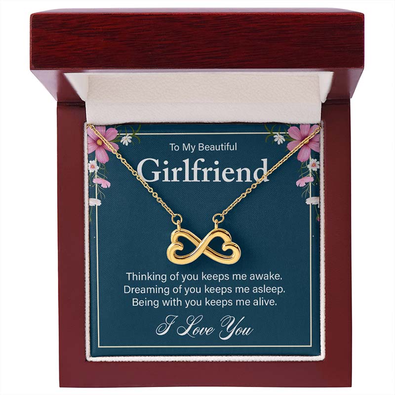 Gold infinity heart necklace displayed with a sentimental message card for girlfriend, inside an open luxury wooden gift box.