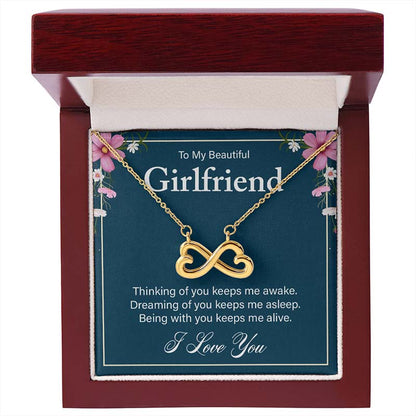 Gold infinity heart necklace displayed with a sentimental message card for girlfriend, inside an open luxury wooden gift box.
