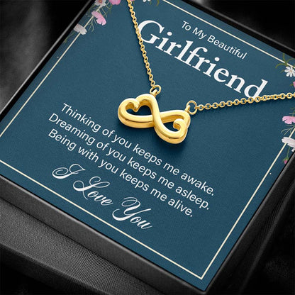 Angled view of a gold infinity heart necklace displayed inside a classic black gift box with a girlfriend message card.